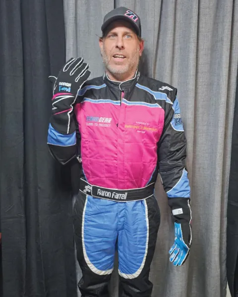 A driver waving in a custom pink and blue suit with matching gloves