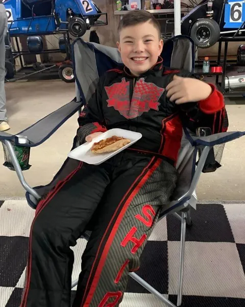 Young driver Shane Shirk smiling in a camping chair at the track in his custom suit